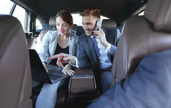 Two business travellers working on a laptop in the back seat of a chauffeur car