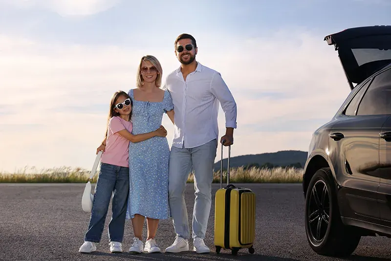 A family with a suitcase beside an SUV on a country road